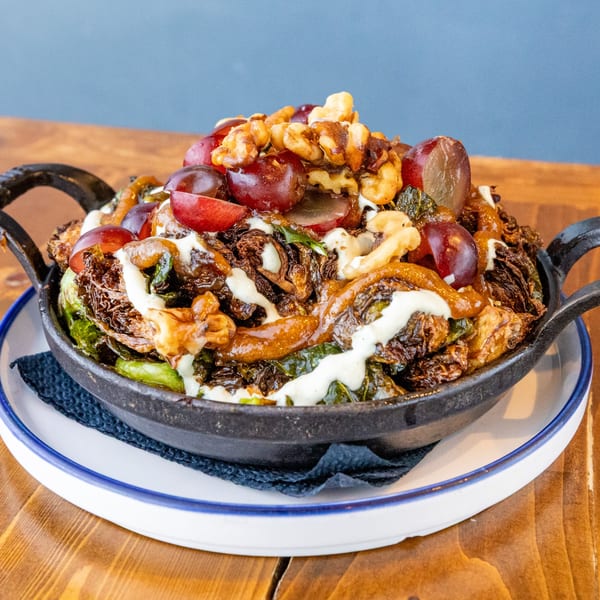 Crispy brussels sprouts with grapes, walnuts, and a creamy sauce in a black skillet.