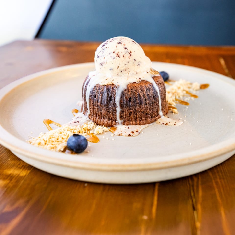 Warm chocolate lava cake with melting vanilla ice cream, blueberries, and caramel drizzle on a plate.
