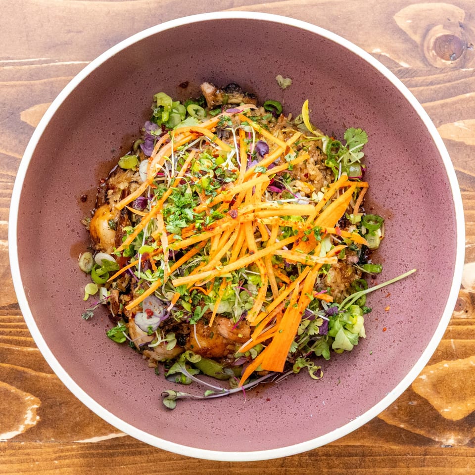 Caribbean dish in a purple bowl, topped with shredded carrots, herbs, and microgreens.