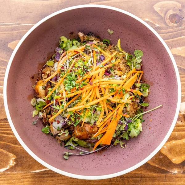 A vibrant Caribbean dish with chicken, rice, and fresh herbs, topped with shredded carrots, in a purple bowl.