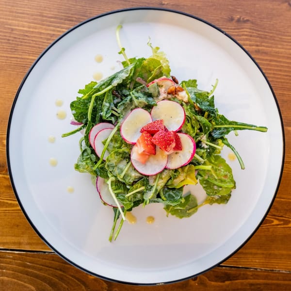 A vibrant Caribbean salad with greens, sliced radishes, and strawberries on a white plate.