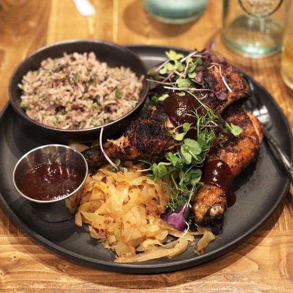 Caribbean jerk chicken with rice, sautéed cabbage, and barbecue sauce on a black plate.