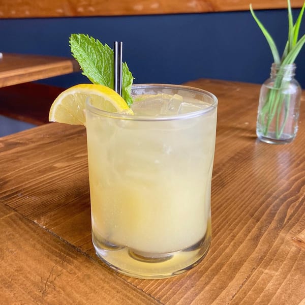 Refreshing Caribbean cocktail with lemon, mint, and straws on a wooden table.
