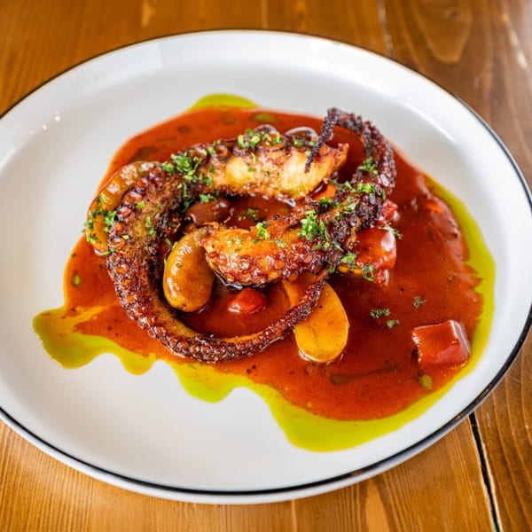 Grilled octopus tentacles with red sauce, green oil, and potato slices on a white plate.