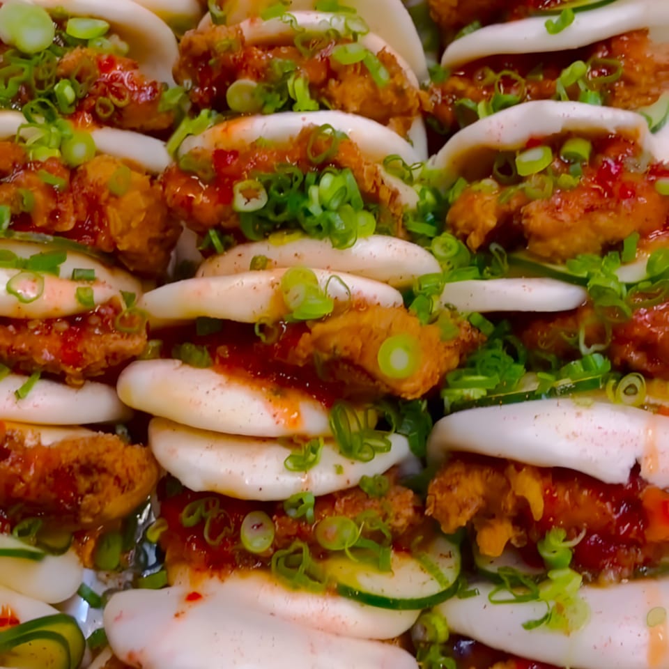 Close-up of Caribbean fried chicken bao buns with red sauce, cucumber, and green onions.
